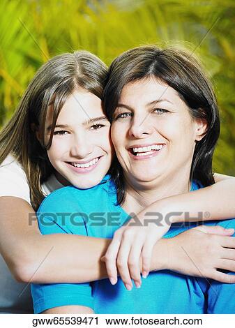 Stock Image - Close-up of a teenage girl hugging her mother from behind. Fotosearch