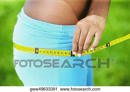 Stock Image - Close-up of a woman measuring her hips with a tape measure. Fotosearch