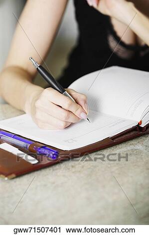 Stock Image - Close-up of a woman's hand writing in a diary. Fotosearch