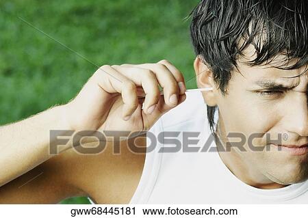 Stock Image - Close-up of a young man cleaning his ear with a cotton swab. Fotosearch