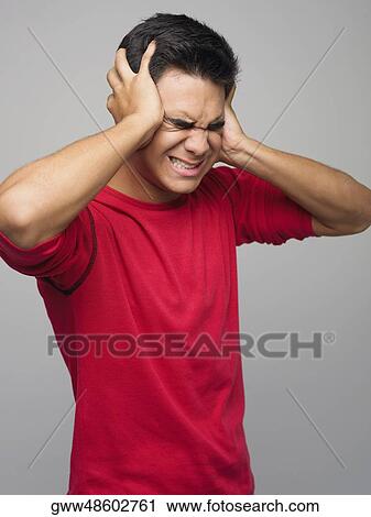 Stock Image - Close-up of a young man covering his ears. Fotosearch