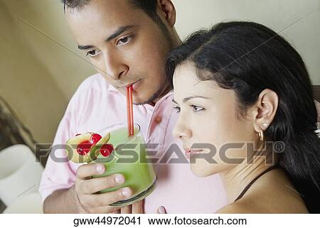 Stock Image - Close-up of a young man drinking juice with a young woman beside him. Fotosearch