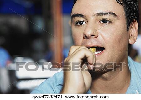 Stock Image - Close-up of a young man eating French fries. Fotosearch