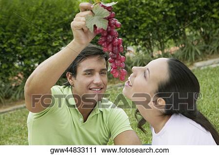 Close-up of a young man holding a bunch of grapes with a young woman eating it View Large Photo Image Stock Image - Close-up of a young man holding a bunch of grapes with a young woman eating it. Fotosearch