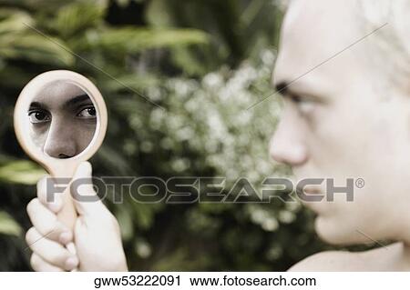 Stock Image - Close-up of a young man holding a vanity mirror. Fotosearch