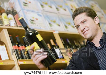 Stock Image - Close-up of a young man holding a wine bottle in a liquor store. Fotosearch