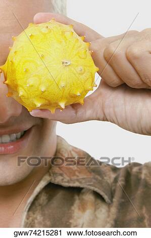 Stock Image - Close-up of a young man holding two kawani fruits on his eyes. Fotosearch