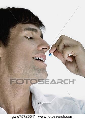 Stock Image - Close-up of a young man taking a capsule. Fotosearch
