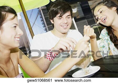 Stock Image - Close-up of a young man with two young women sharing an ice-cream sundae. Fotosearch