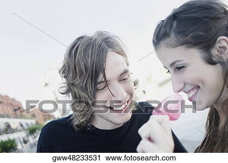 Stock Image - Close-up of a young woman eating an ice-cream with a teenage boy smiling. Fotosearch