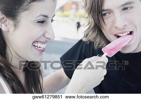 Stock Image - Close-up of a young woman feeding an ice-cream to a teenage boy. Fotosearch