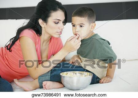 Stock Image - Close-up of a young woman feeding her son popcorn. Fotosearch