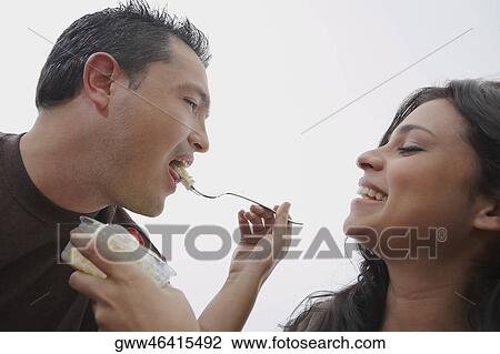 Stock Image - Close-up of a young woman feeding ice-cream to a mid adult man. Fotosearch