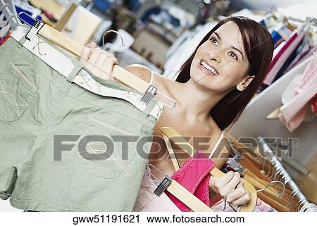 Stock Image - Close-up of a young woman holding clothes on a hanger in a clothing store. Fotosearch