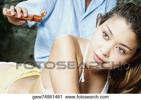 Close-up of a young woman lying down with a man pouring suntan lotion on her back View Large Photo Image Stock Image - Close-up of a young woman lying down with a man pouring suntan lotion on her back. Fotosearch