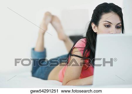 Close-up of a young woman lying on the bed and using a laptop View Large Photo Image Stock Image - Close-up of a young woman lying on the bed and using a laptop. Fotosearch