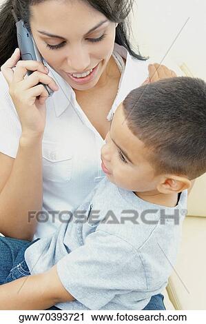 Stock Image - Close-up of a young woman on the phone and her son sitting on her lap. Fotosearch