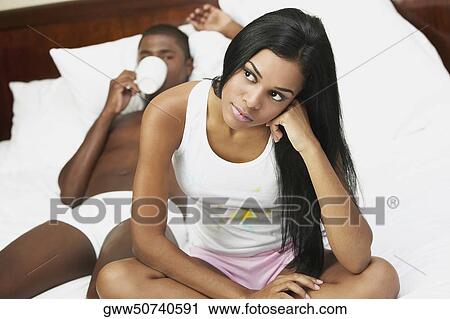 Close-up of a young woman sitting with her head in her hand and a mid adult man lying in the background View Large Photo Image Stock Image - Close-up of a young woman sitting with her head in her hand and a mid adult man lying in the background. Fotosearch