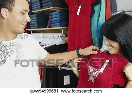 Close-up of a young woman trying on clothes in a clothing store with a young man looking at her View Large Photo Image Stock Image - Close-up of a young woman trying on clothes in a clothing store with a young man looking at her. Fotosearch