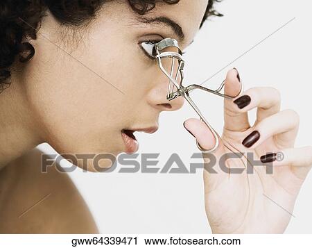 Stock Image - Close-up of a young woman using an eyelash curler. Fotosearch