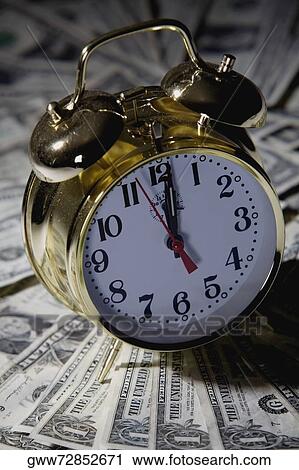 Stock Image - Close-up of an alarm clock on paper currency. Fotosearch