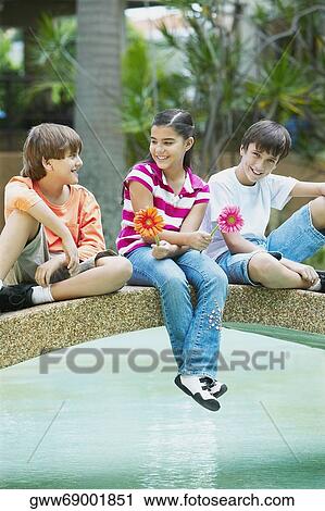 Girl sitting between two boys on a footbridge across a pond View Large Photo Image Stock Image - Girl sitting between two boys on a footbridge across a pond. Fotosearch
