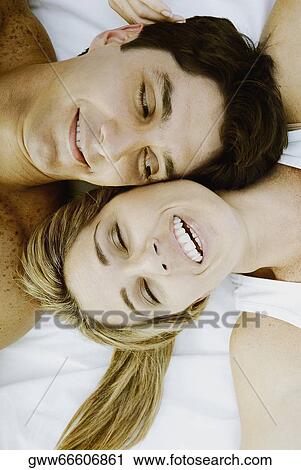 Stock Image - High angle view of a mid adult couple lying on the bed and smiling. Fotosearch