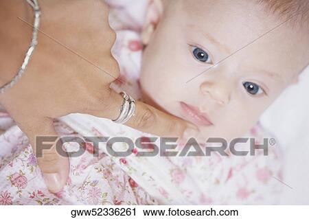 Stock Image - High angle view of a woman's finger touching the chin of a baby girl. Fotosearch