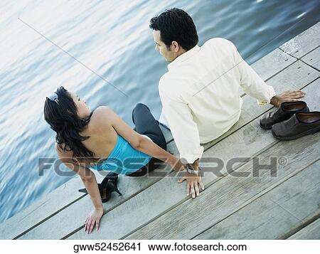 High angle view of a young couple sitting on a pier View Large Photo Image Stock Image - High angle view of a young couple sitting on a pier. Fotosearch