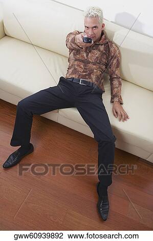 Stock Image - High angle view of a young man using a remote control. Fotosearch
