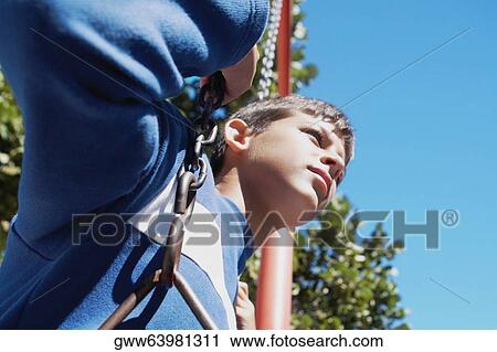 Low angle view of a teenage boy on a swing View Large Photo Image Stock Image - Low angle view of a teenage boy on a swing. Fotosearch