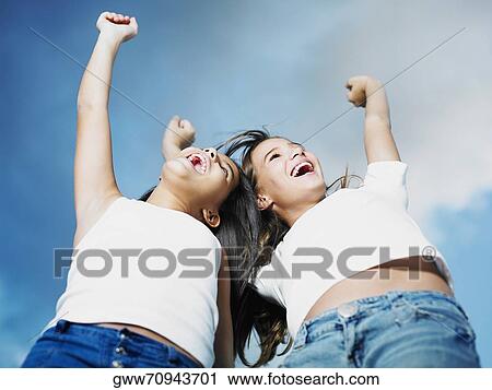 Low angle view of a teenage girl and her sister with their arms raised View Large Photo Image Stock Image - Low angle view of a teenage girl and her sister with their arms raised. Fotosearch