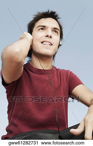 Stock Image - Low angle view of a young man listening to music. Fotosearch