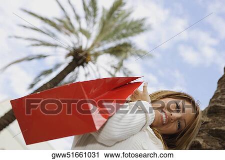 Low angle view of a young woman holding a shopping bag and smiling View Large Photo Image Stock Image - Low angle view of a young woman holding a shopping bag and smiling. Fotosearch