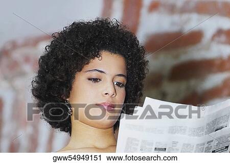 Stock Image - Low angle view of a young woman reading a newspaper. Fotosearch