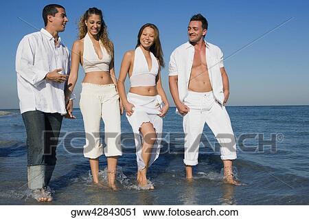 Stock Image - Low angle view of two young women and a young man with a mid adult man walking on the beach. Fotosearch