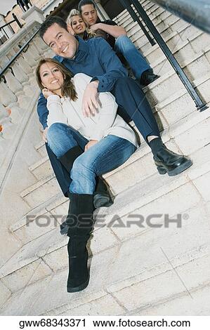 Low angle view of two young women and a young man with a mid adult man sitting on steps and smiling View Large Photo Image Stock Image - Low angle view of two young women and a young man with a mid adult man sitting on steps and smiling. Fotosearch