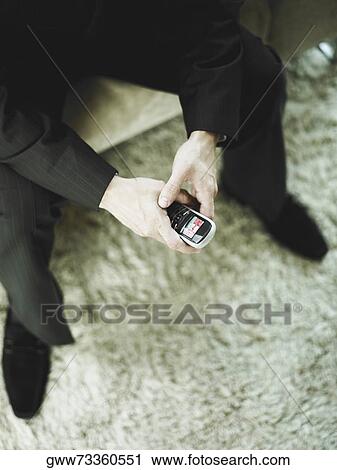 Stock Image - Low section view of a businessman holding a mobile phone. Fotosearch