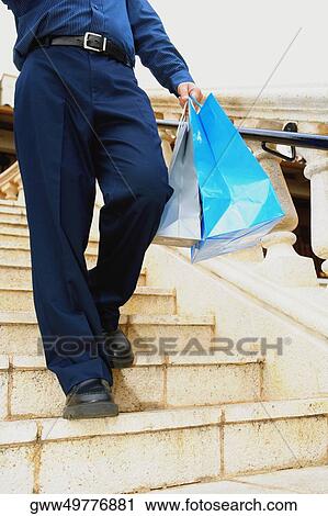 Stock Image - Low section view of a man moving down on steps and carrying shopping bags. Fotosearch