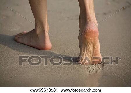 Stock Image - Low section view of a person walking on the beach. Fotosearch