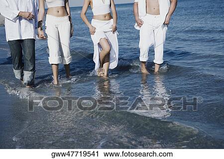 Stock Image - Low section view of two couples walking on the beach. Fotosearch