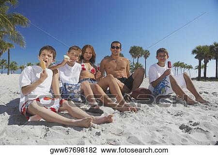 Mid adult man and a young man sitting with their children on the beach View Large Photo Image Stock Image - Mid adult man and a young man sitting with their children on the beach. Fotosearch
