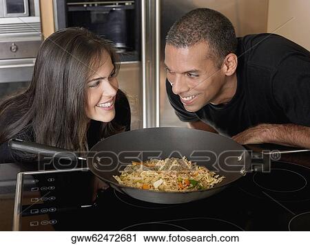 Stock Image - Mid adult man and a young woman looking at each other behind a kitchen counter. Fotosearch