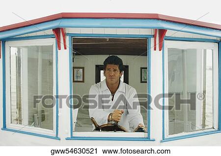 Stock Image - Mid adult man holding the helm of a motorboat. Fotosearch