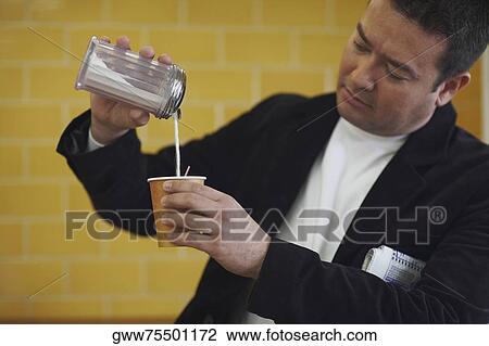 Stock Image - Mid adult man pouring milk into a disposable cup. Fotosearch