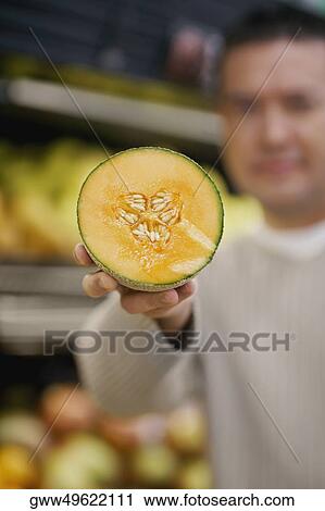 Stock Image - Mid adult man showing the cross section of a cantaloupe. Fotosearch
