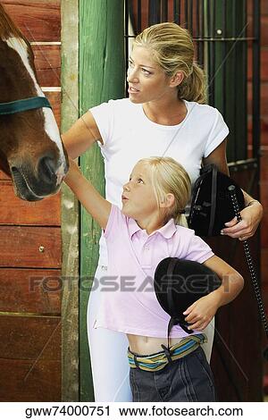 Stock Image - Mid adult woman and her daughter standing in a stable. Fotosearch