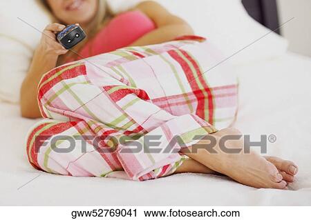 Stock Image - Mid adult woman lying on the bed and watching television. Fotosearch
