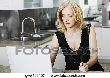 Mid adult woman using a laptop in a kitchen View Large Photo Image Stock Image - Mid adult woman using a laptop in a kitchen. Fotosearch