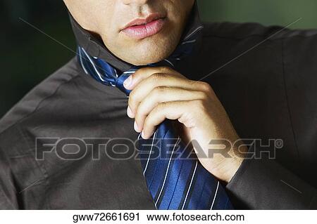 Stock Image - Mid section view of a businessman adjusting his tie. Fotosearch